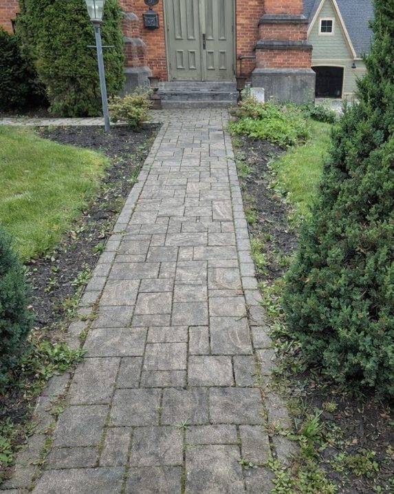A paver walkway, dark and dirty, leading to a front door