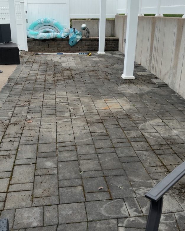 A paver patio under a pergola, dark with dirt