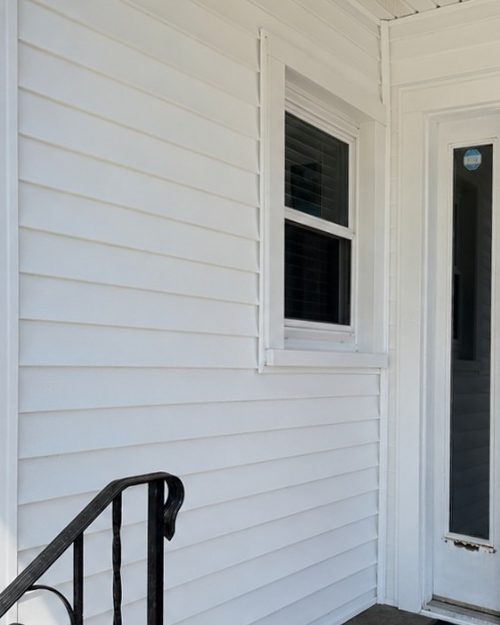 The same entry after washing, clean white siding beside a red door